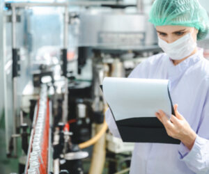 food and beverage manufacturing - lady with clipboard in beverage plant wearing white overalls, mask and hair net